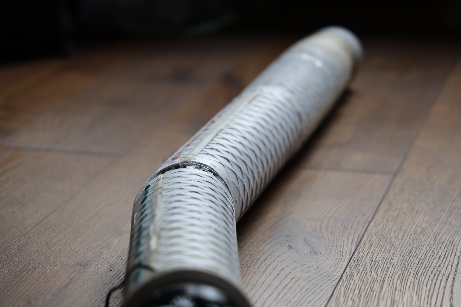 The long flexible kirigami robot bent across a wood floor.